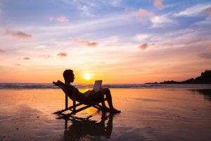 man on computer on beach at sunset