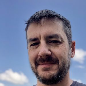 Man with facial hair with clouds and sky behind